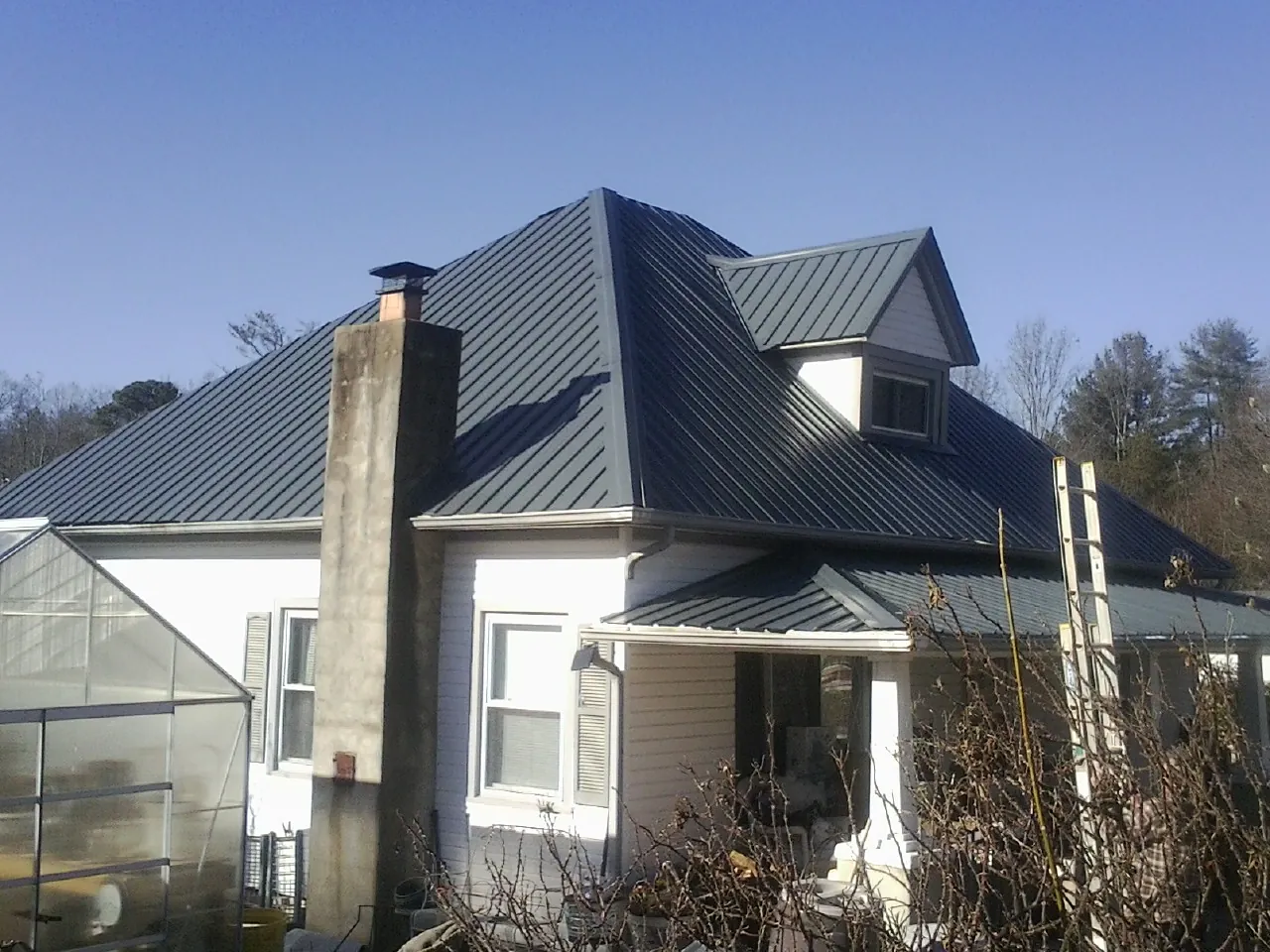 Dark blue standing seam metal roof on a white farmhouse with dormer — Slate & Tile Roof Repair by Roofing Brothers in Hellier