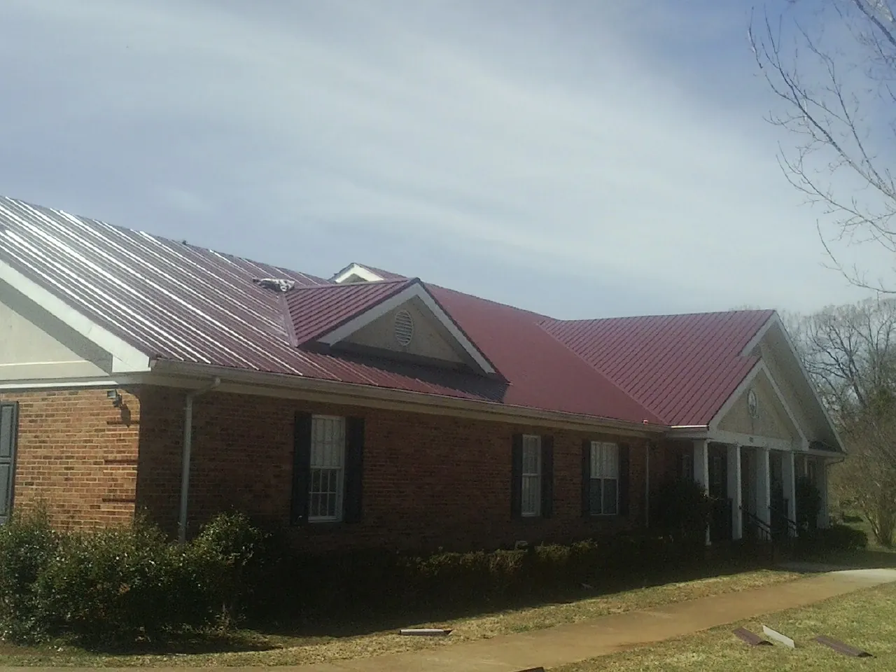 Red metal roof with gabled entries on a long brick building, from a Hail Damage Roof Repair job in Hellier