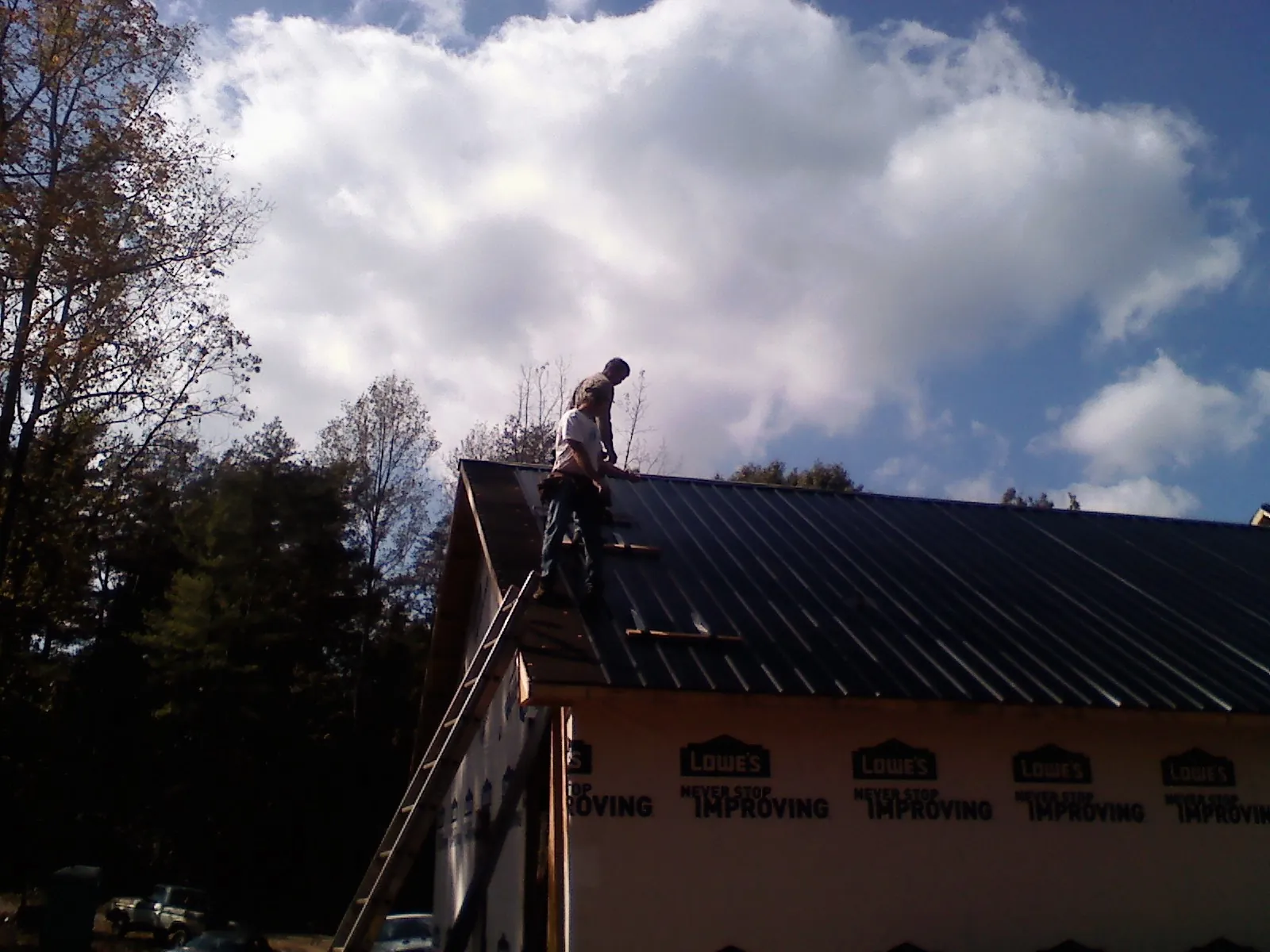 Roofer fastening dark metal panels high against a cloudy sky, from a Roof Inspection job in Hellier