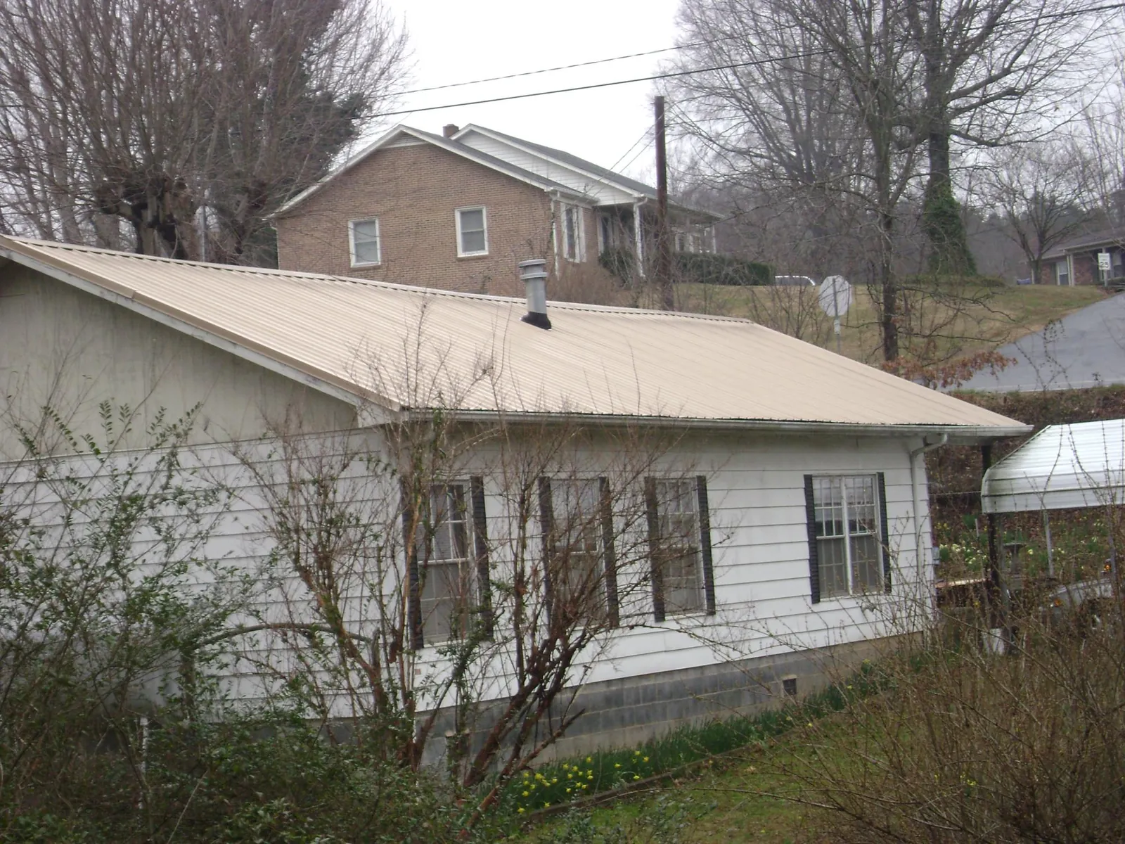 Tan metal roof on a white sided house set into a hillside — Commercial Roofing by Roofing Brothers in Hellier