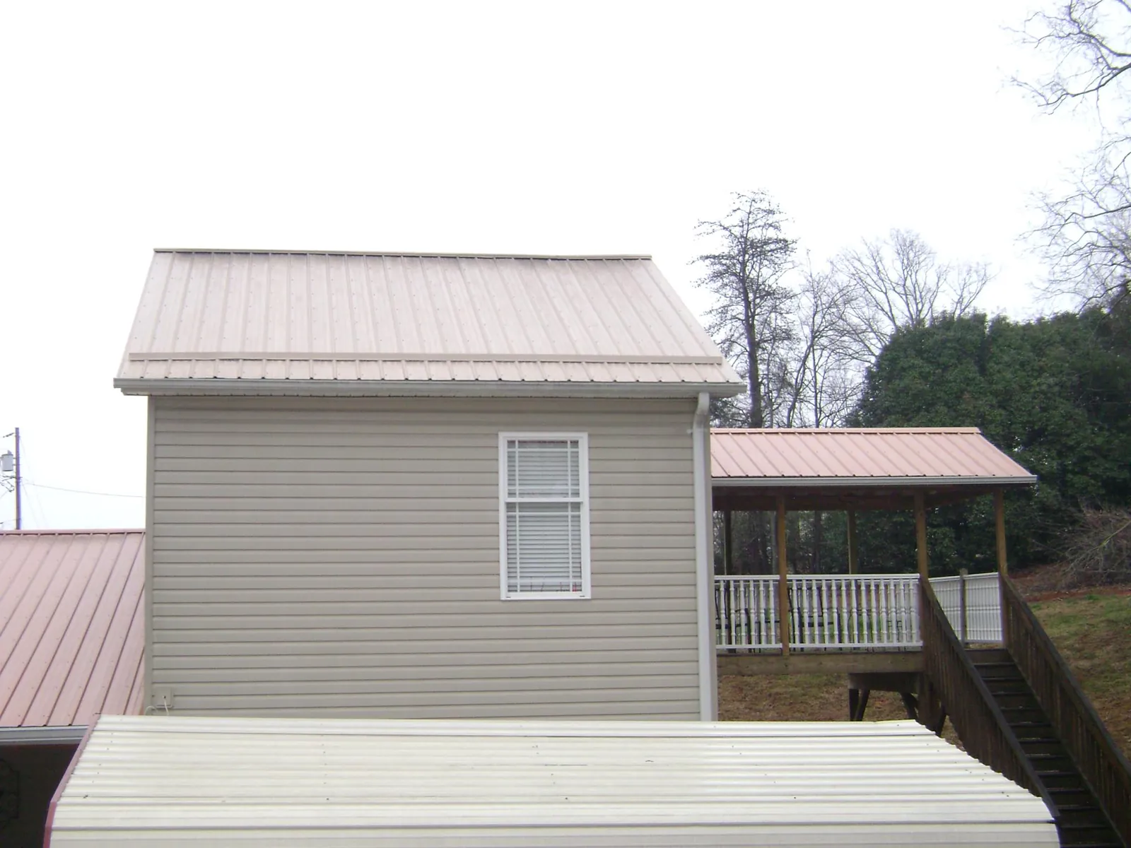 Tan metal roofs on a two story addition and attached porch, from a Roof Replacement job in Hellier